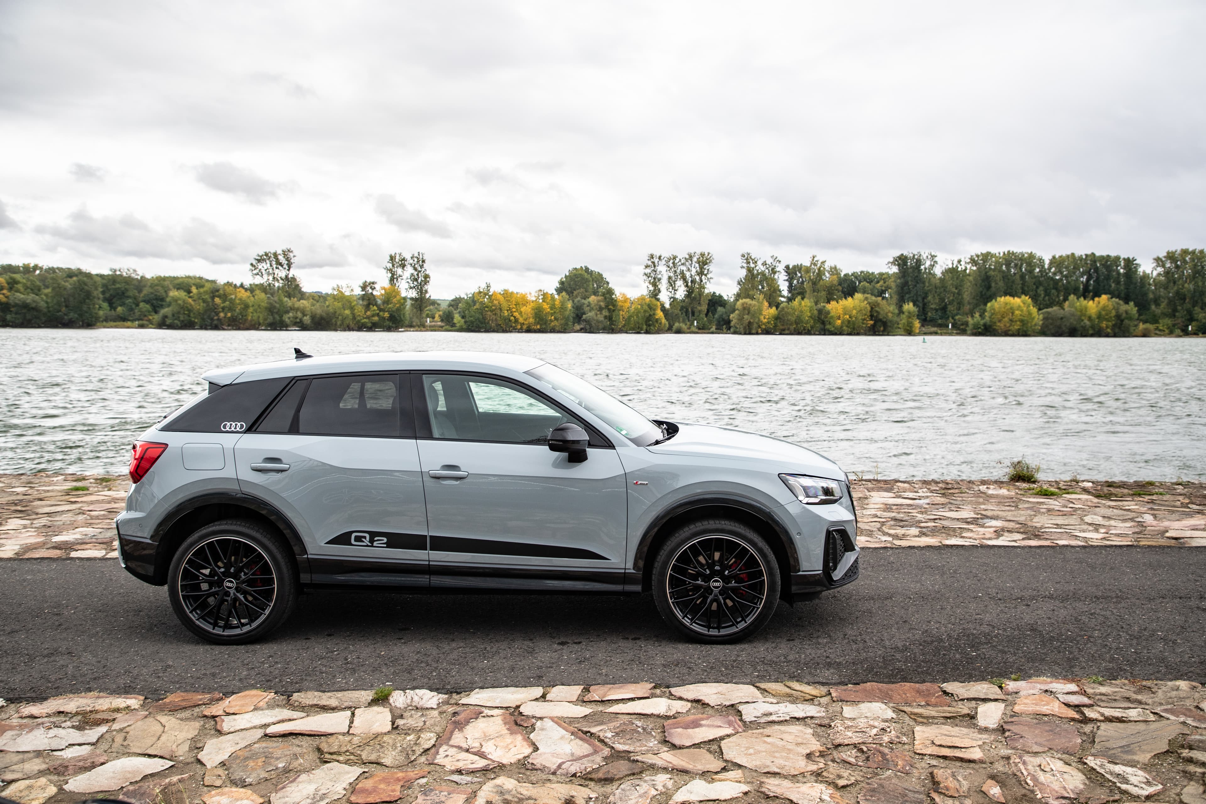 Pilkas Audi Q2 GA, šoninis profilis prie vandens